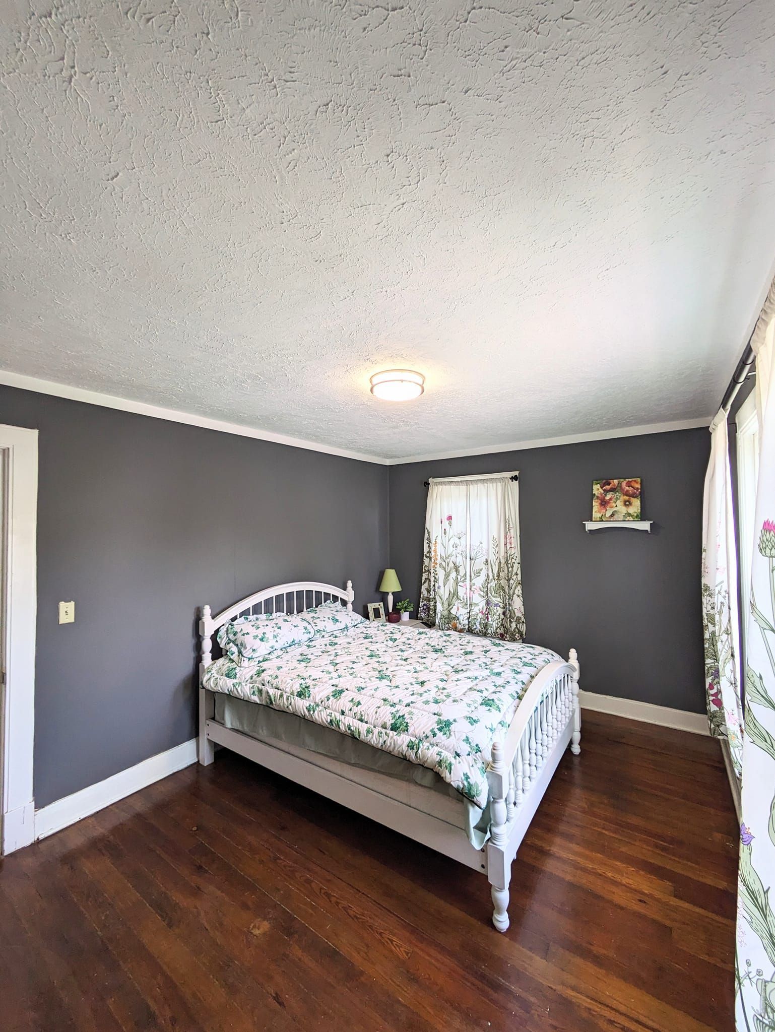 Small bedroom with gray walls, white ceiling, hardwood floor, and a white bed with floral bedding.