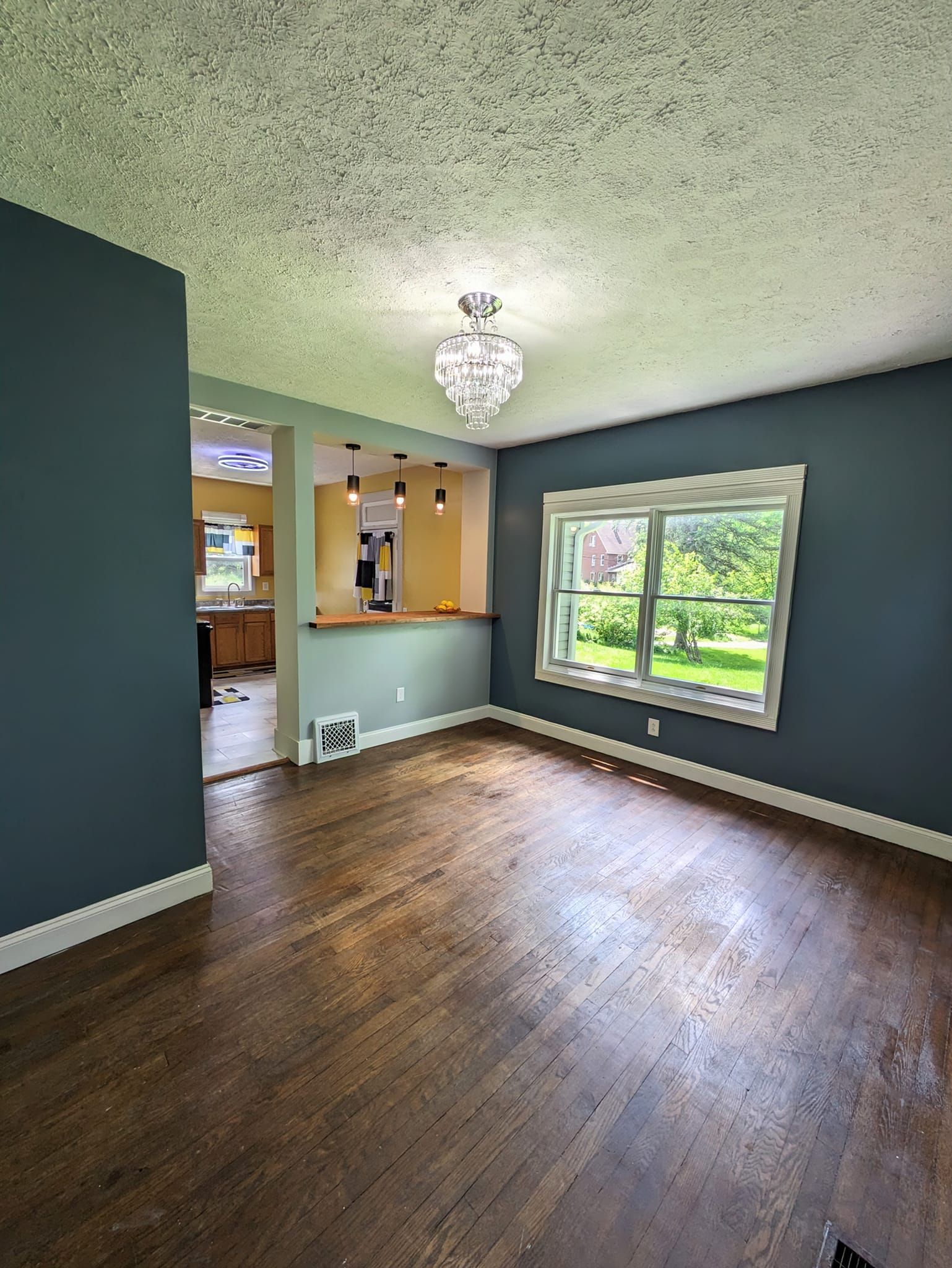 Empty room with hardwood floors, gray walls, a window, and a chandelier.