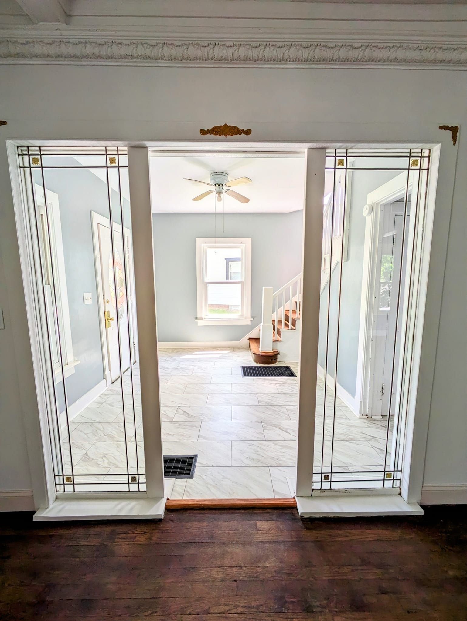 Open white double doors to a bright room with a ceiling fan, window, and tiled floor