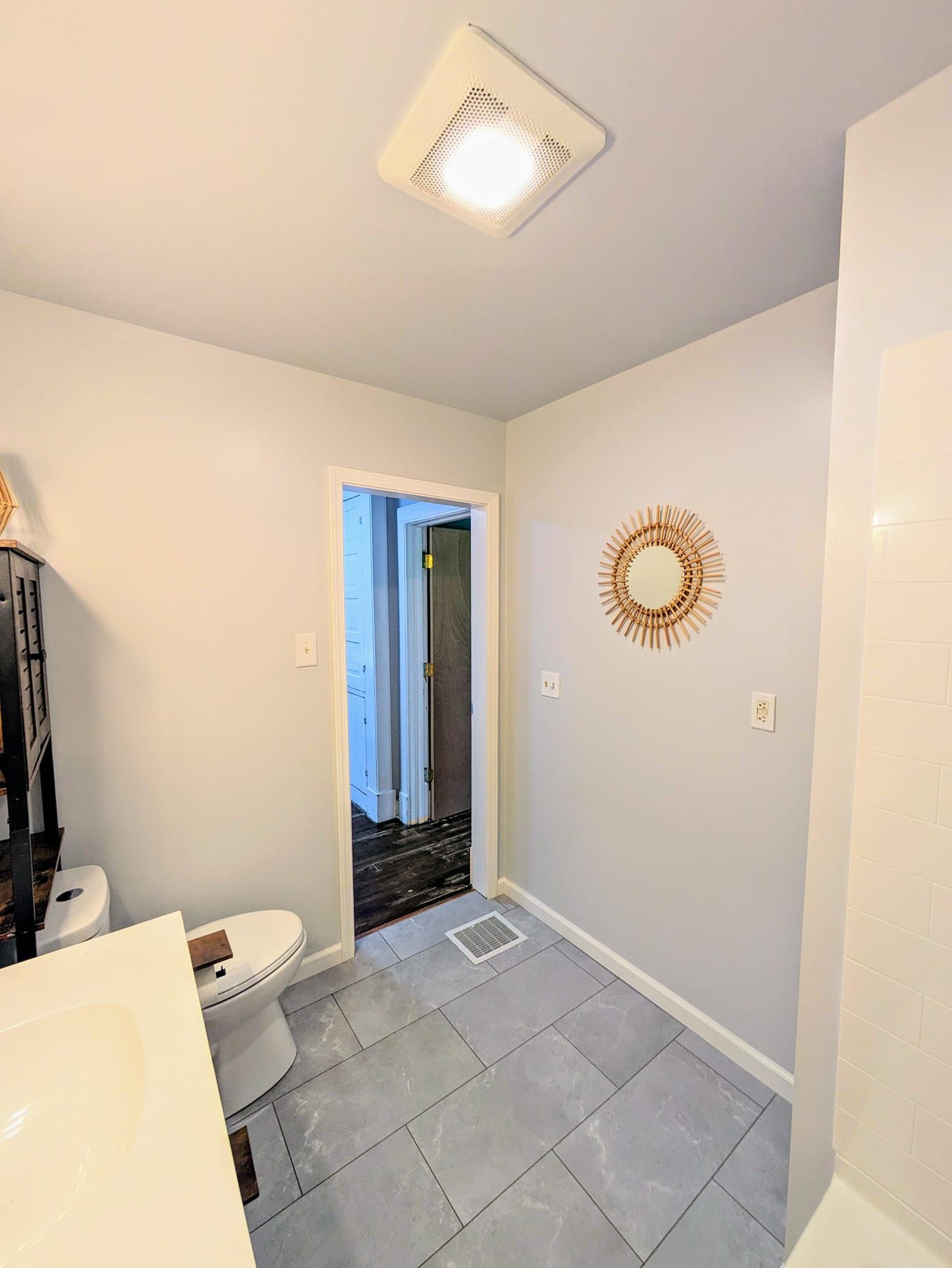 Small tiled hallway with a ceiling light, wall mirror, and open doorway to a bathroom.