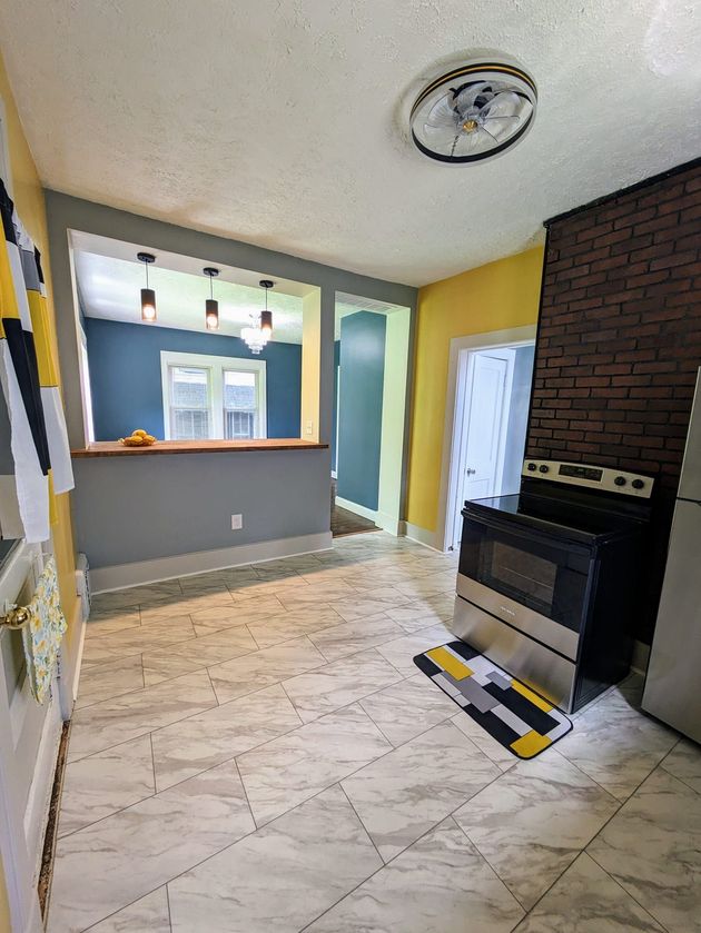 Empty kitchen with light tile floor, brick stove wall, and a pass-through window to another room.