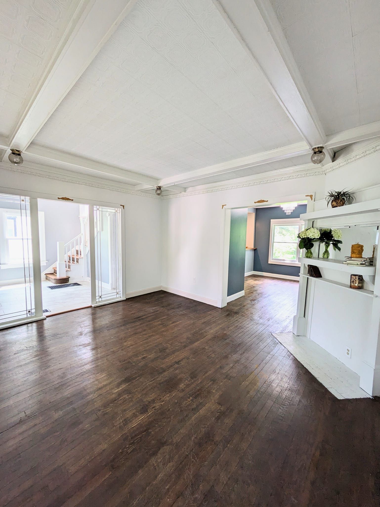 Empty bright room with dark wood floor, vaulted white ceiling, and open sliding glass doors.
