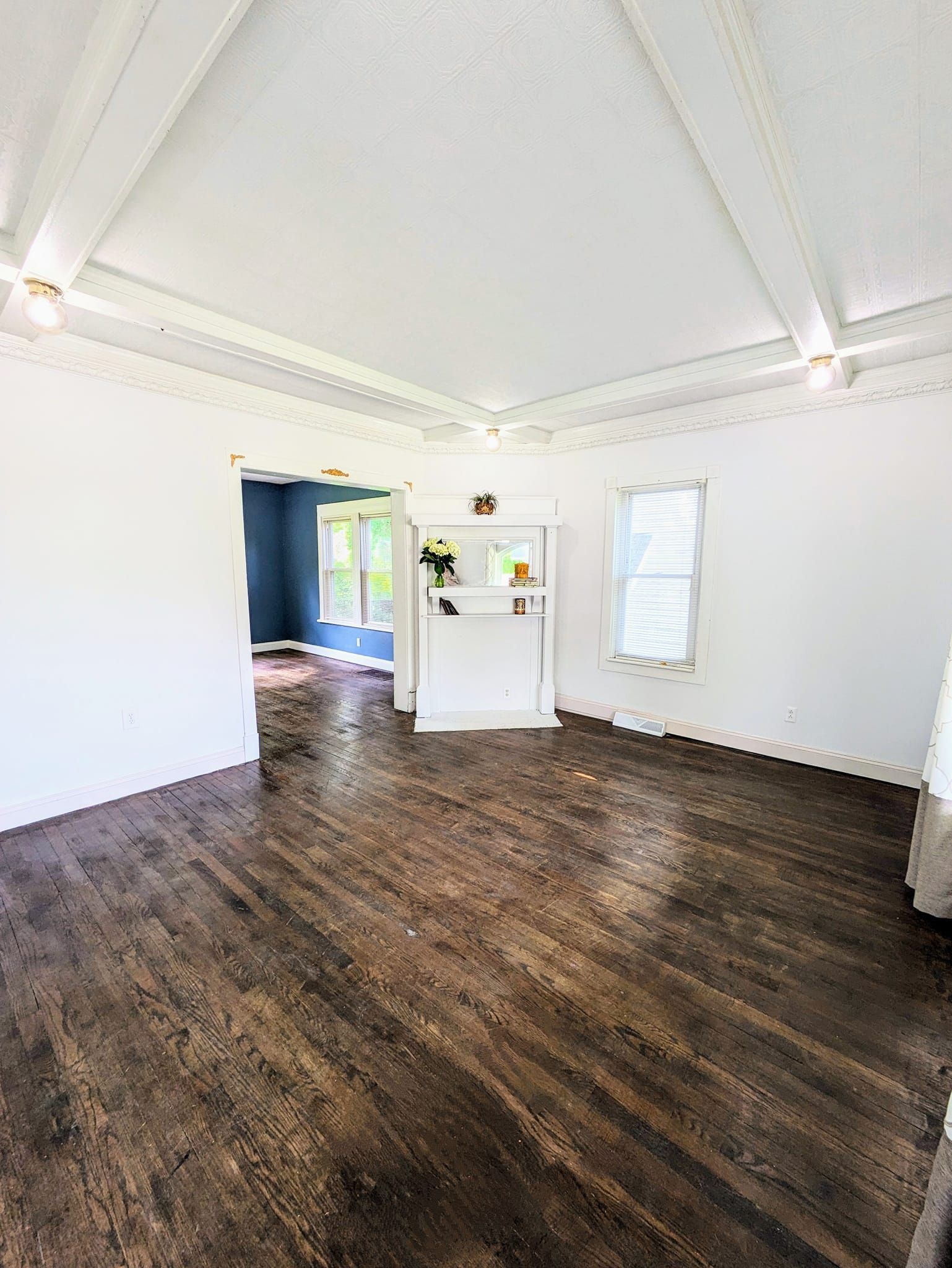 Bright empty room with white walls, dark wood floors, and a small built-in shelf near a doorway.