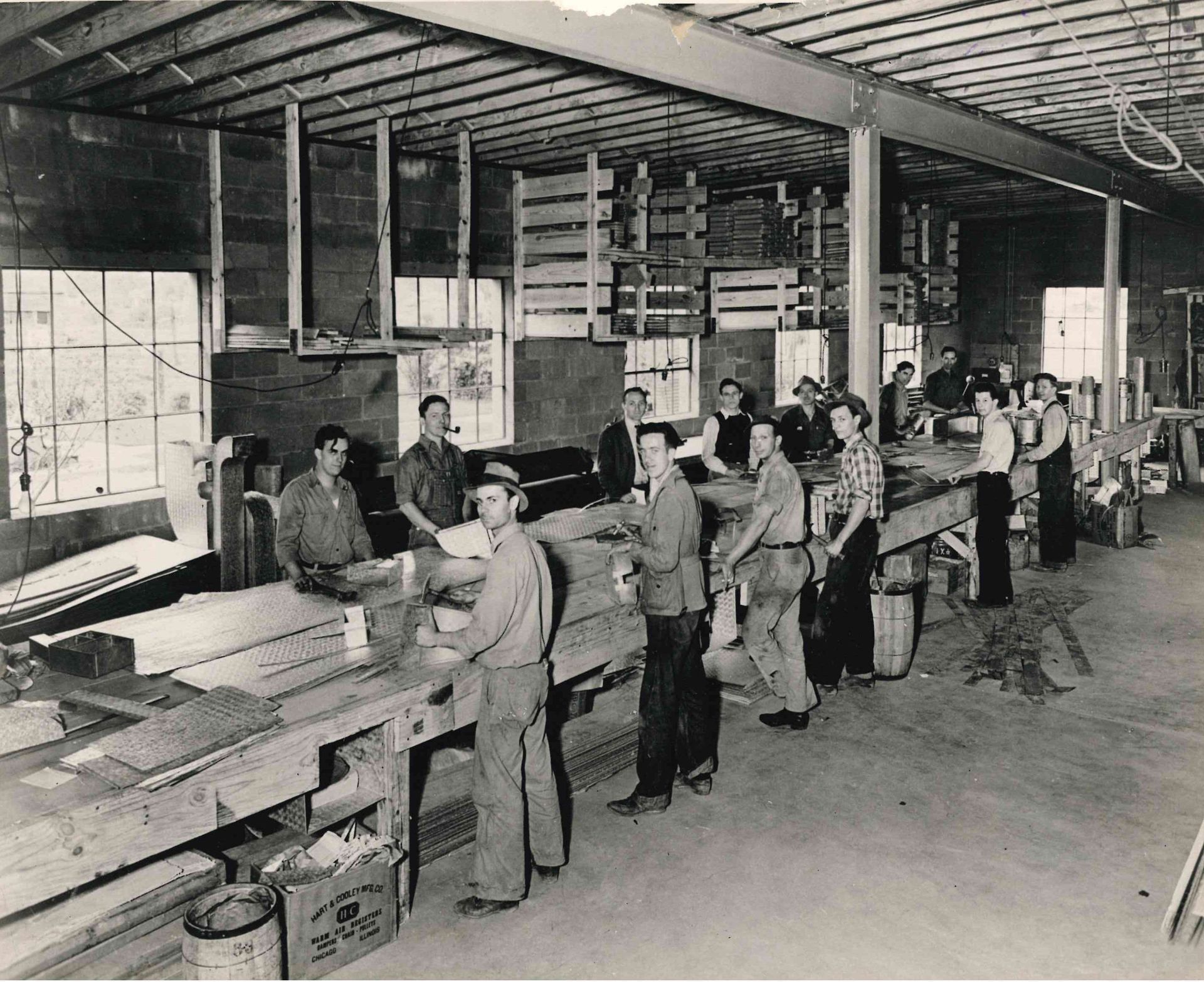 Woodworking shop with workers standing at a long assembly line inside a factory.