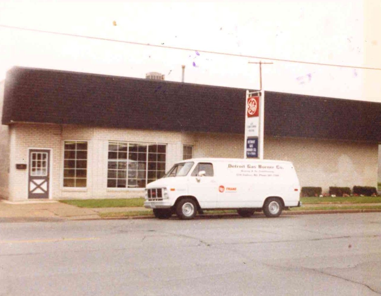 White van parked in front of a low building with a dark roof and a signpost outside.
