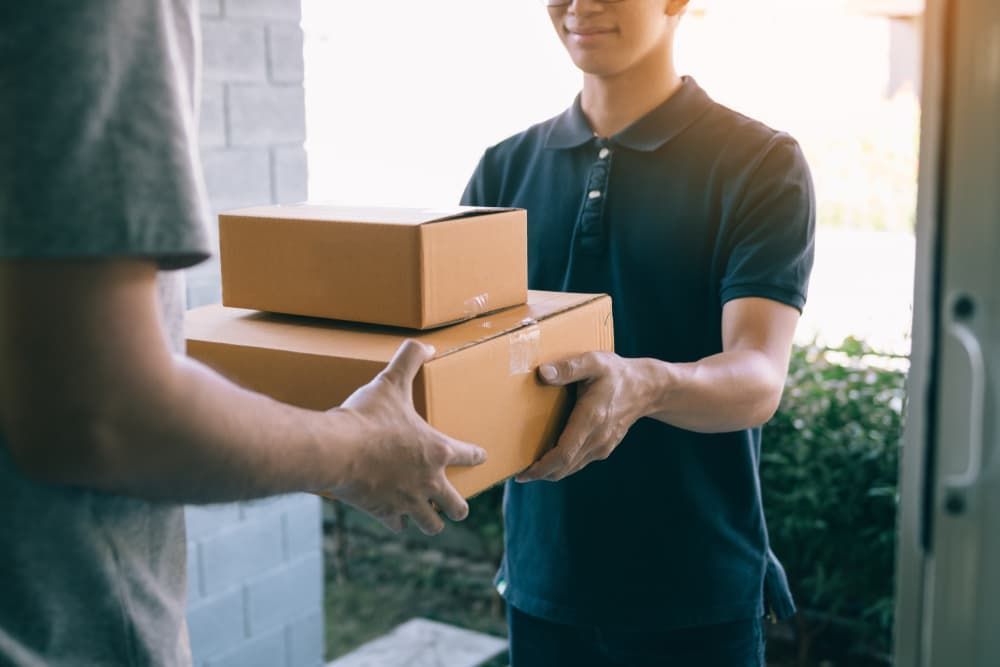 A Delivery Man Is Handing A Package To A Customer — South Burnett Truck Rental  In Chinchilla, QLD