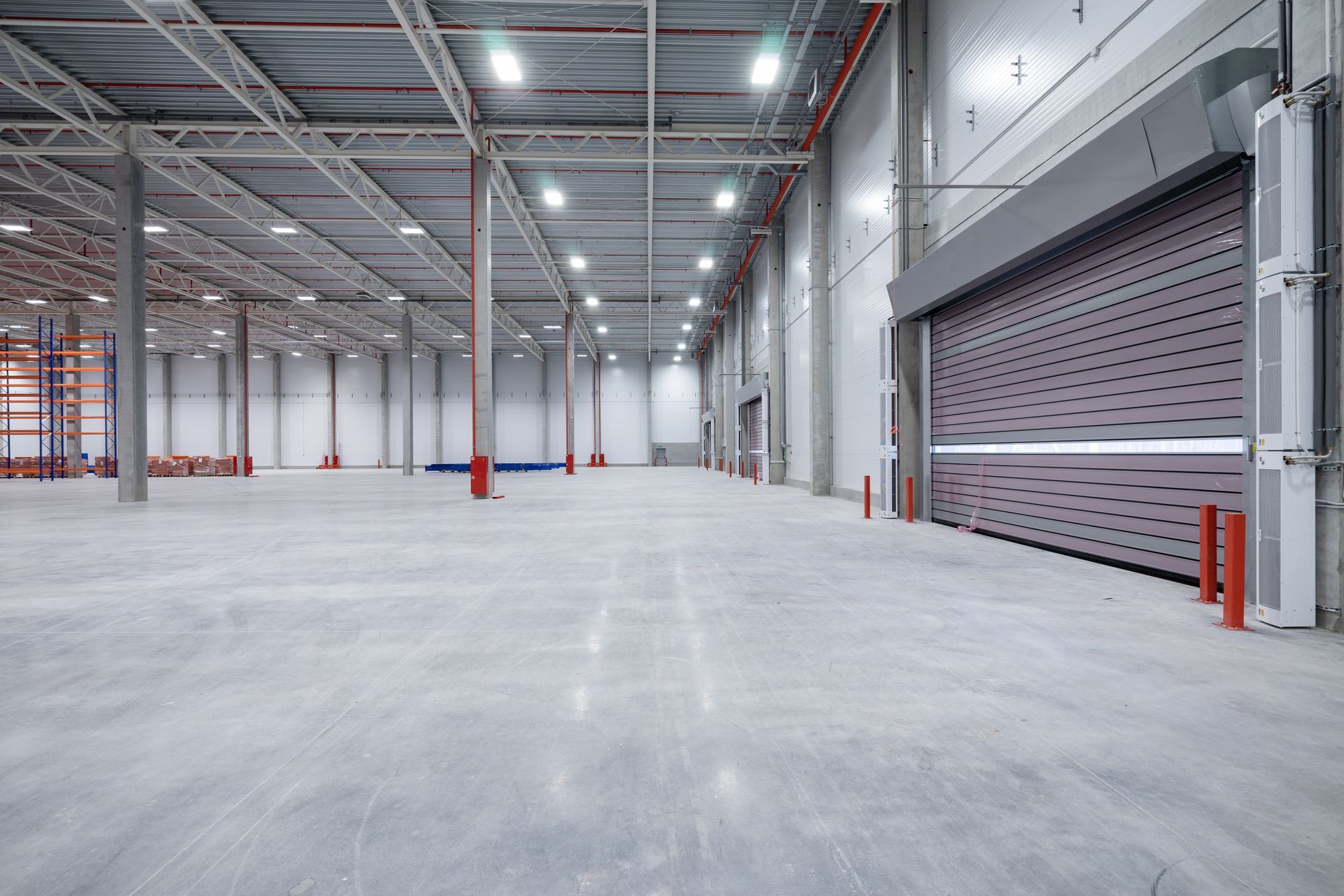 Empty warehouse interior with high ceilings, concrete floor, and closed loading bay doors