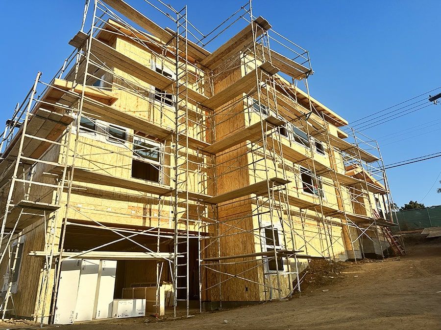 Multi-story building under construction with scaffolding and yellow sheathing under a clear blue sky