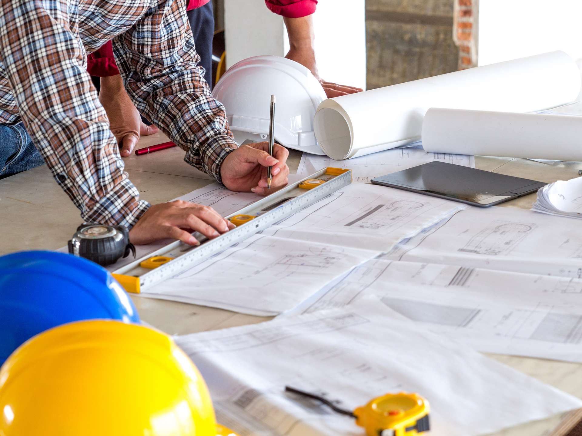 Architects reviewing blueprints at a construction site with hard hats and rolled plans