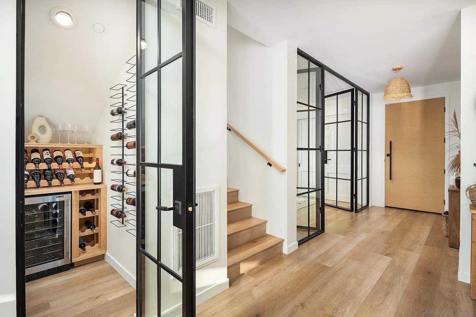 Bright hallway with black glass doors, wooden floors, staircase, and wine storage area
