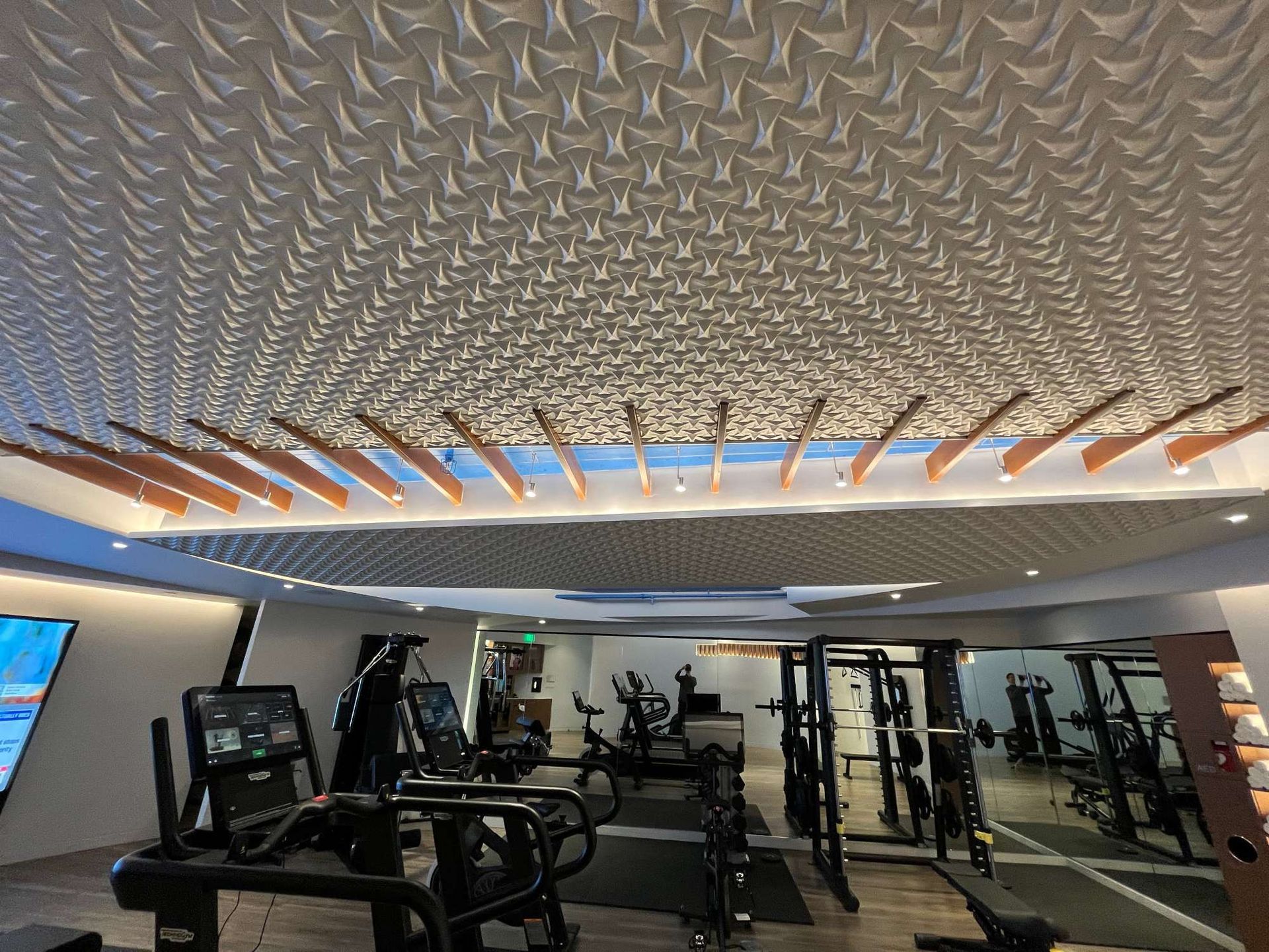 Modern gym interior with treadmills, weight machines, mirrors, and a patterned ceiling lighting strip