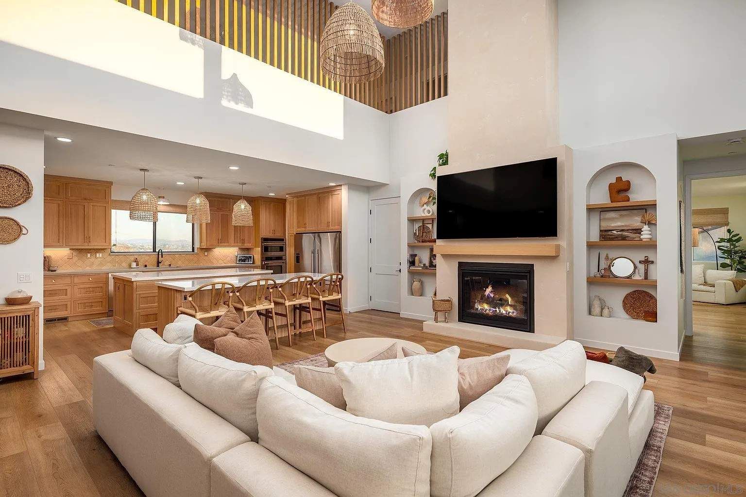 Bright open living room with sectional sofa, fireplace, wall TV, and kitchen island in background
