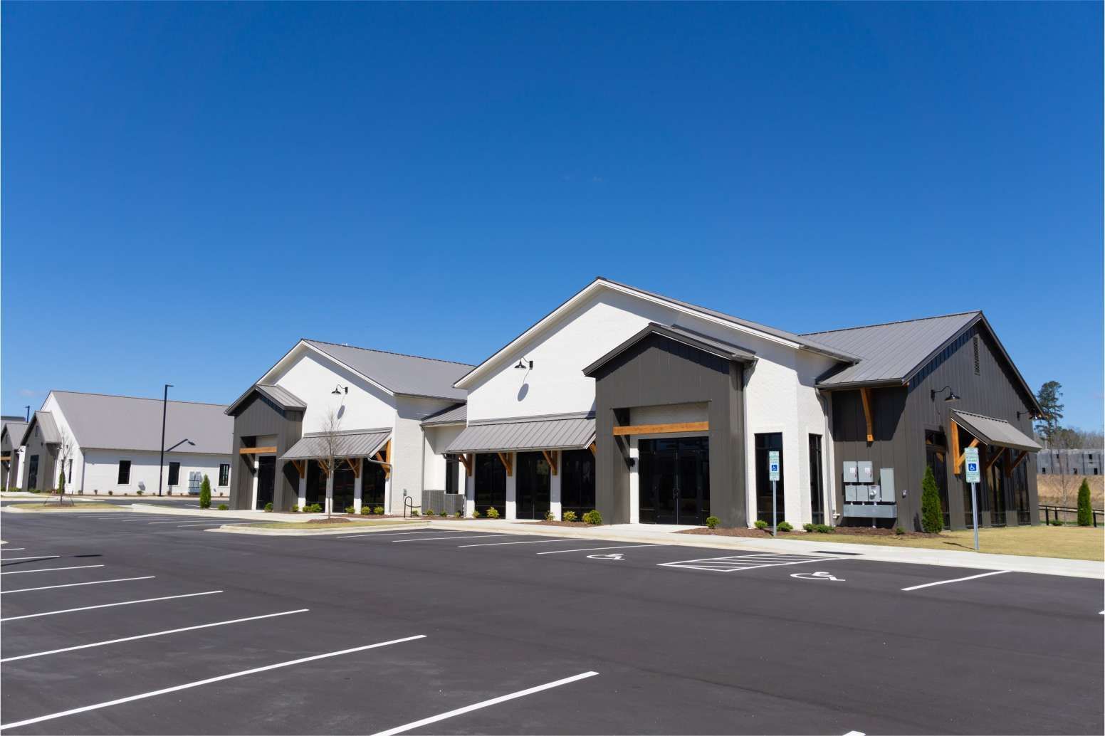 Empty parking lot outside a row of light-colored storefronts under a clear blue sky
