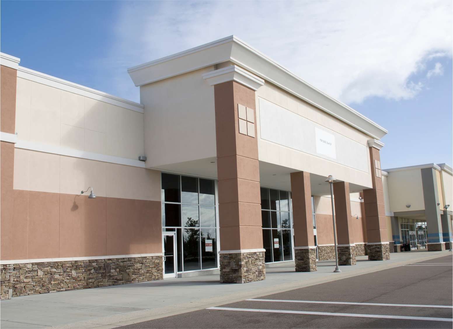 Exterior of a beige and brown storefront with large glass windows and an empty parking lot