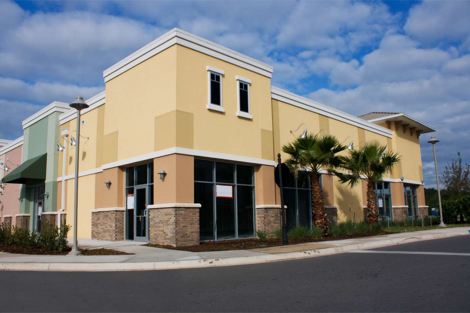 Yellow and beige storefront building on a street corner under a cloudy blue sky