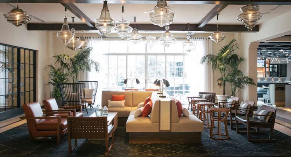 Modern lounge with sofas, armchairs, hanging lights, and large windows in a bright open room