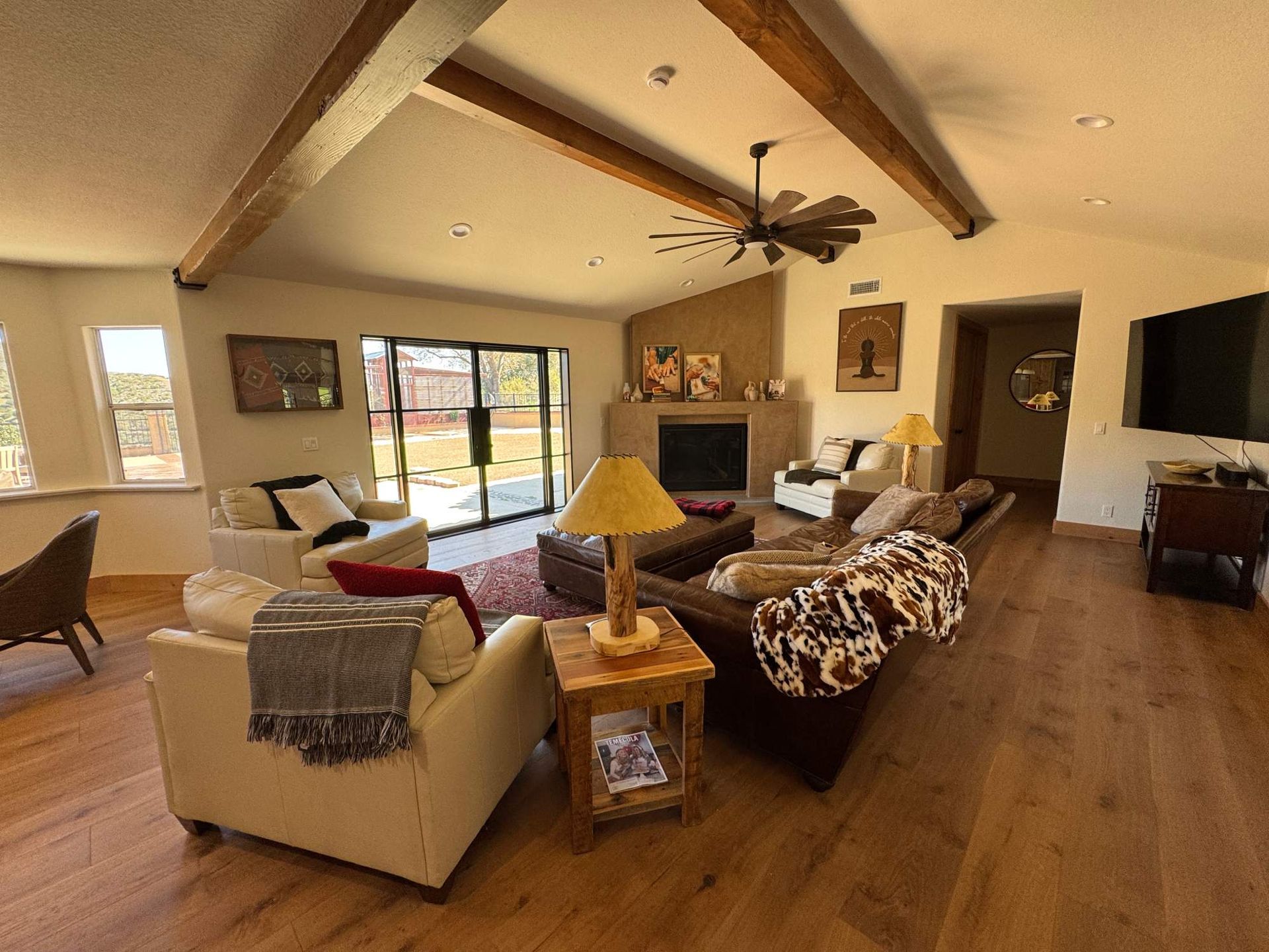 Cozy living room with wood beams, beige sofas, a ceiling fan, and sliding glass doors