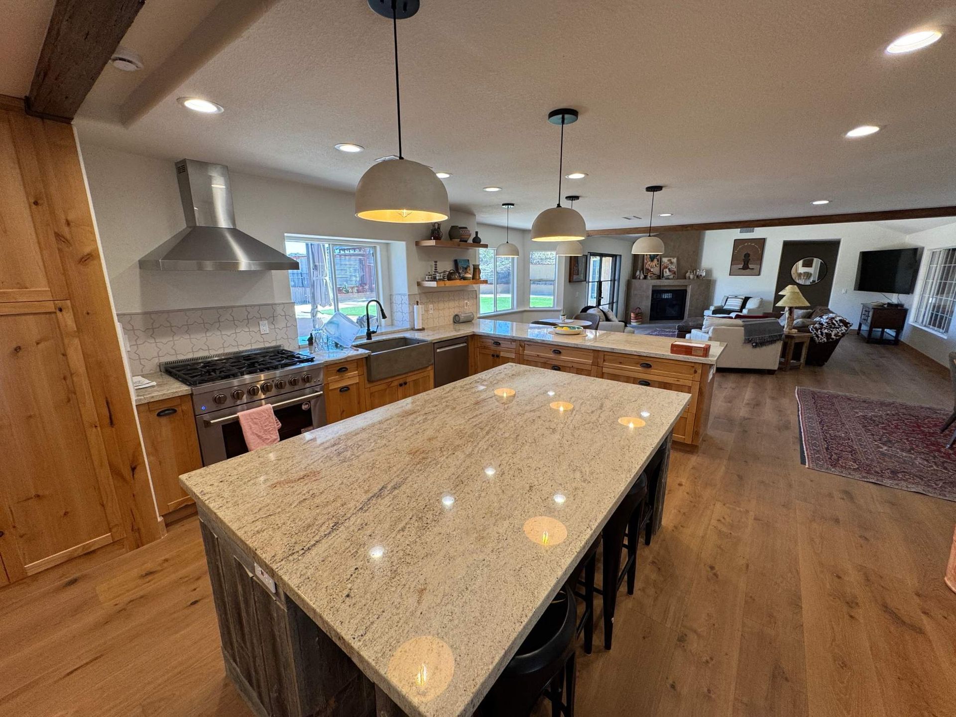 Modern kitchen with large marble island, wooden floors, pendant lights, and open living area