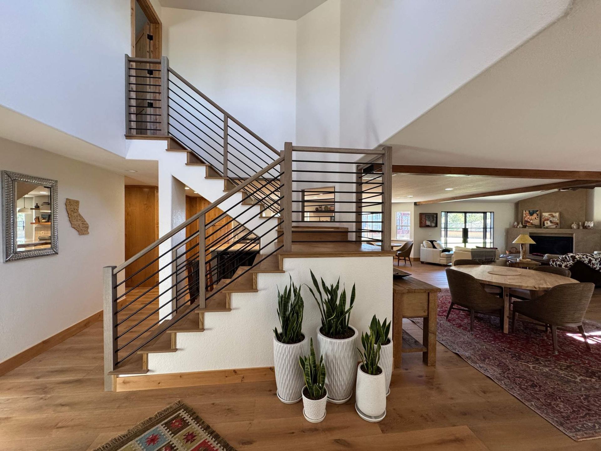 Modern living room with staircase, open railing, and potted plants near the entryway