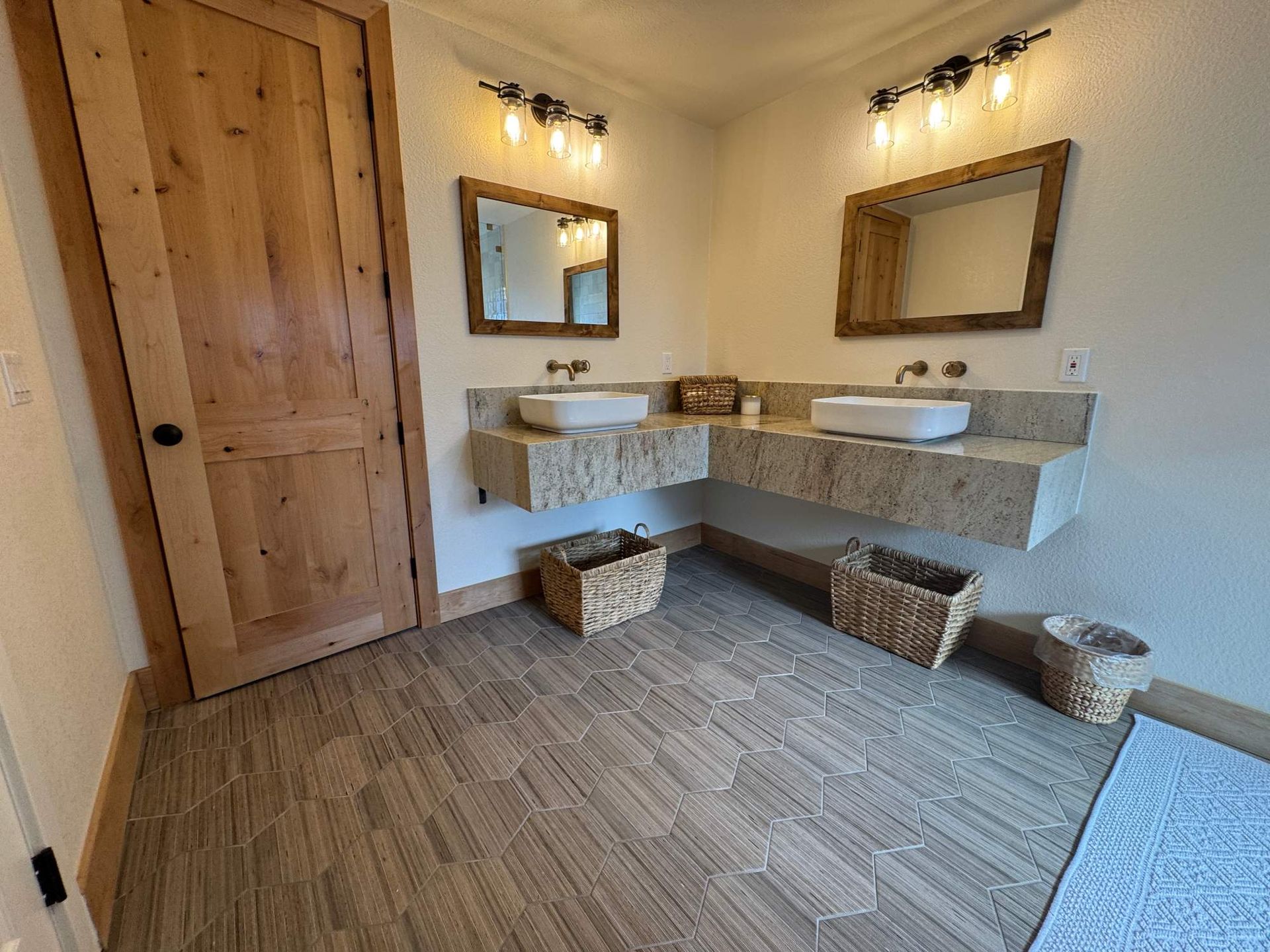 Small rustic bathroom with wood door, dual sinks, mirrors, and woven baskets under the counters.