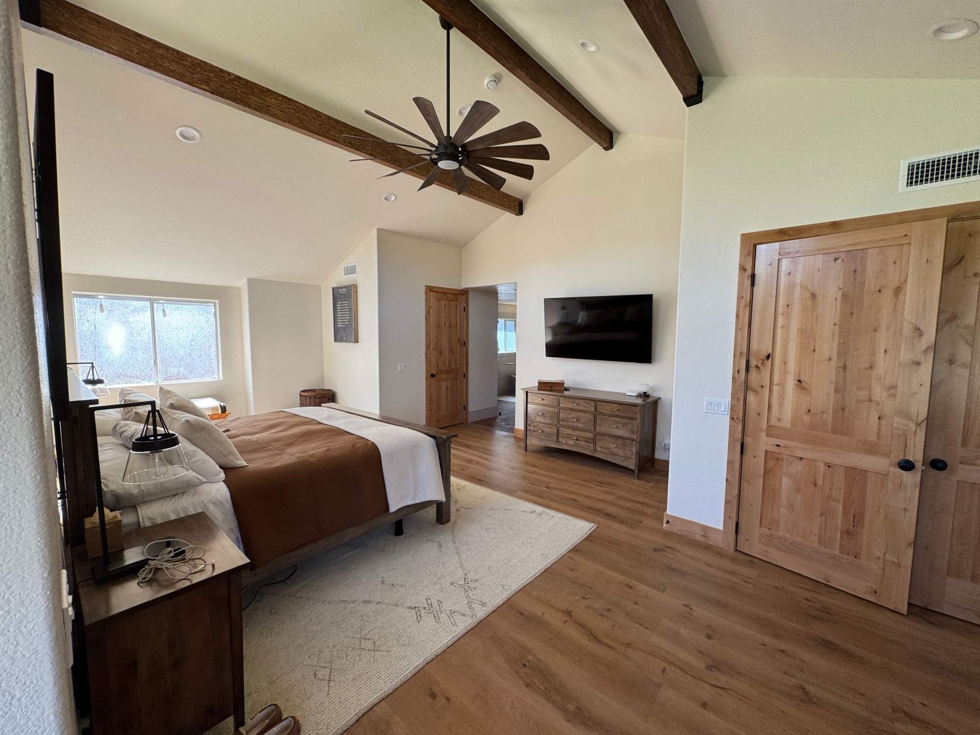 Spacious bedroom with wood floors, vaulted ceiling, large bed, TV, and rustic wooden doors