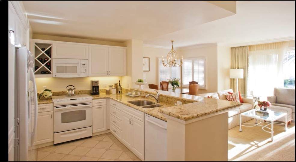 Bright kitchen with white cabinets, granite island, and sunlit dining area beside a large window.