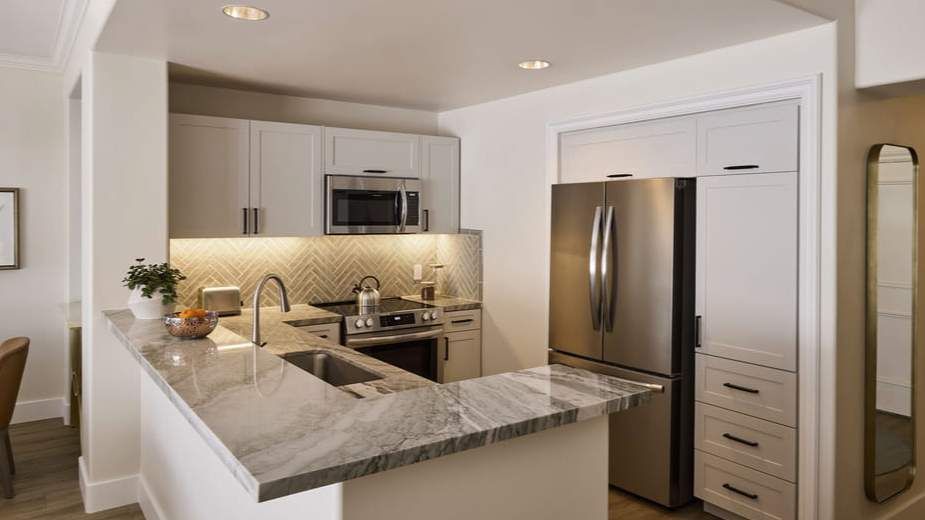 Modern white kitchen with stainless steel appliances, marble island, and under-cabinet lighting