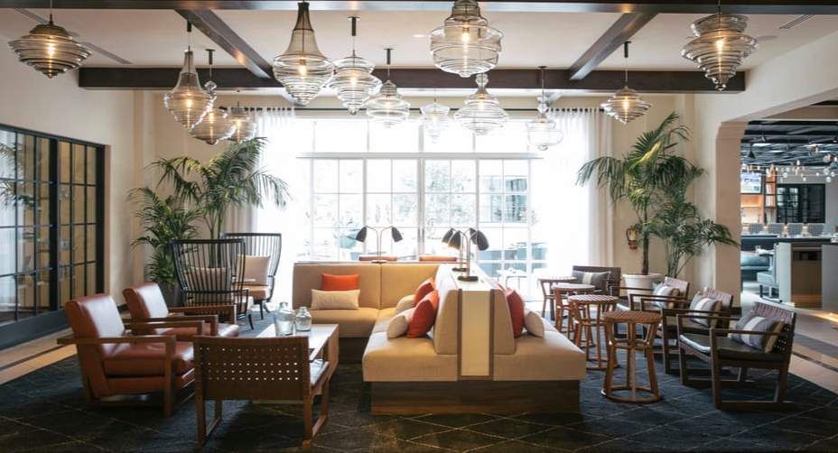 Bright, stylish lounge with sofas, armchairs, tables, hanging lights, and large windows