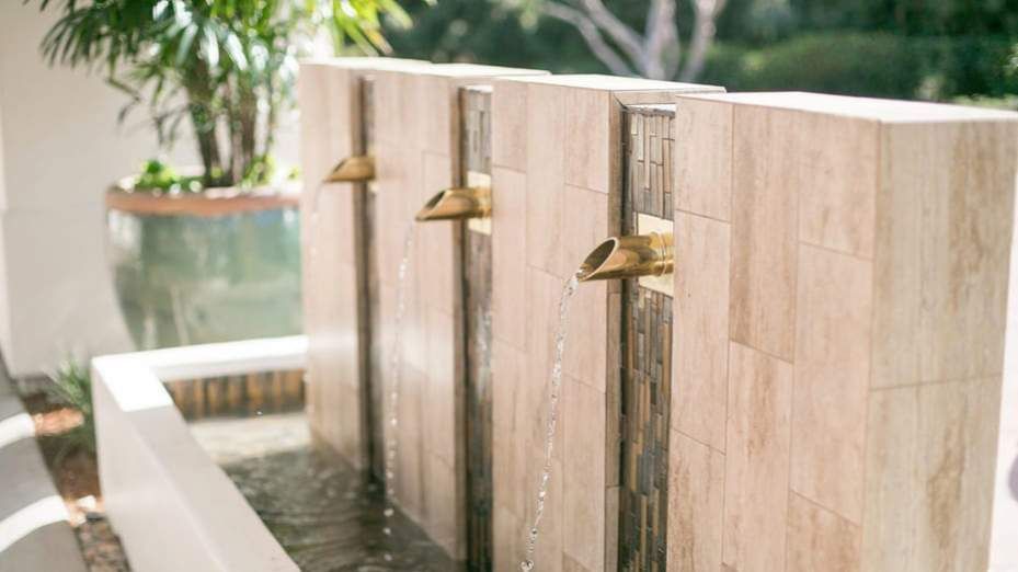 Three gold faucets pouring water from a stone wall into a basin outdoors