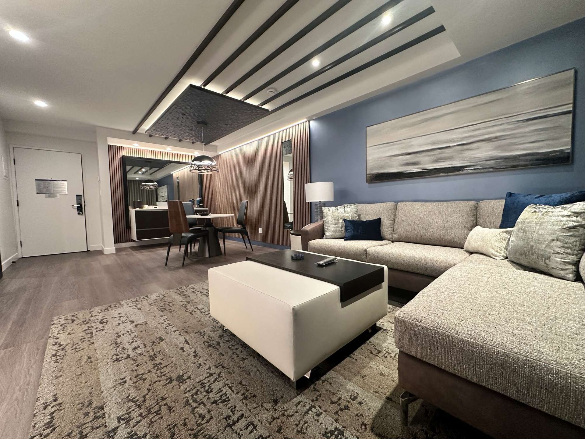Modern living room with blue accent wall, sectional sofa, coffee table, and dining area in back.