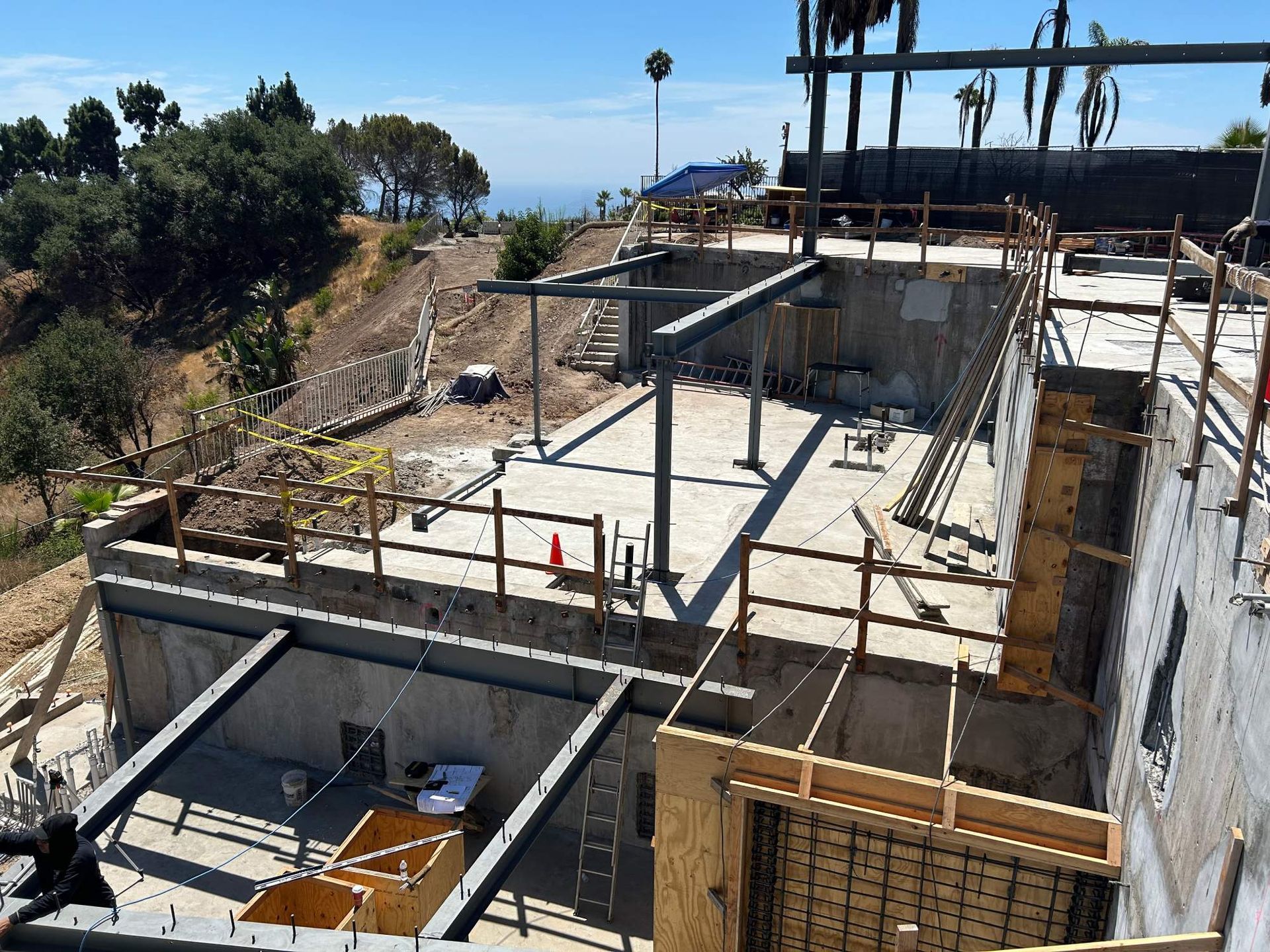 Partially built concrete structure on a hillside overlooking the ocean, with scaffolding and rebar.