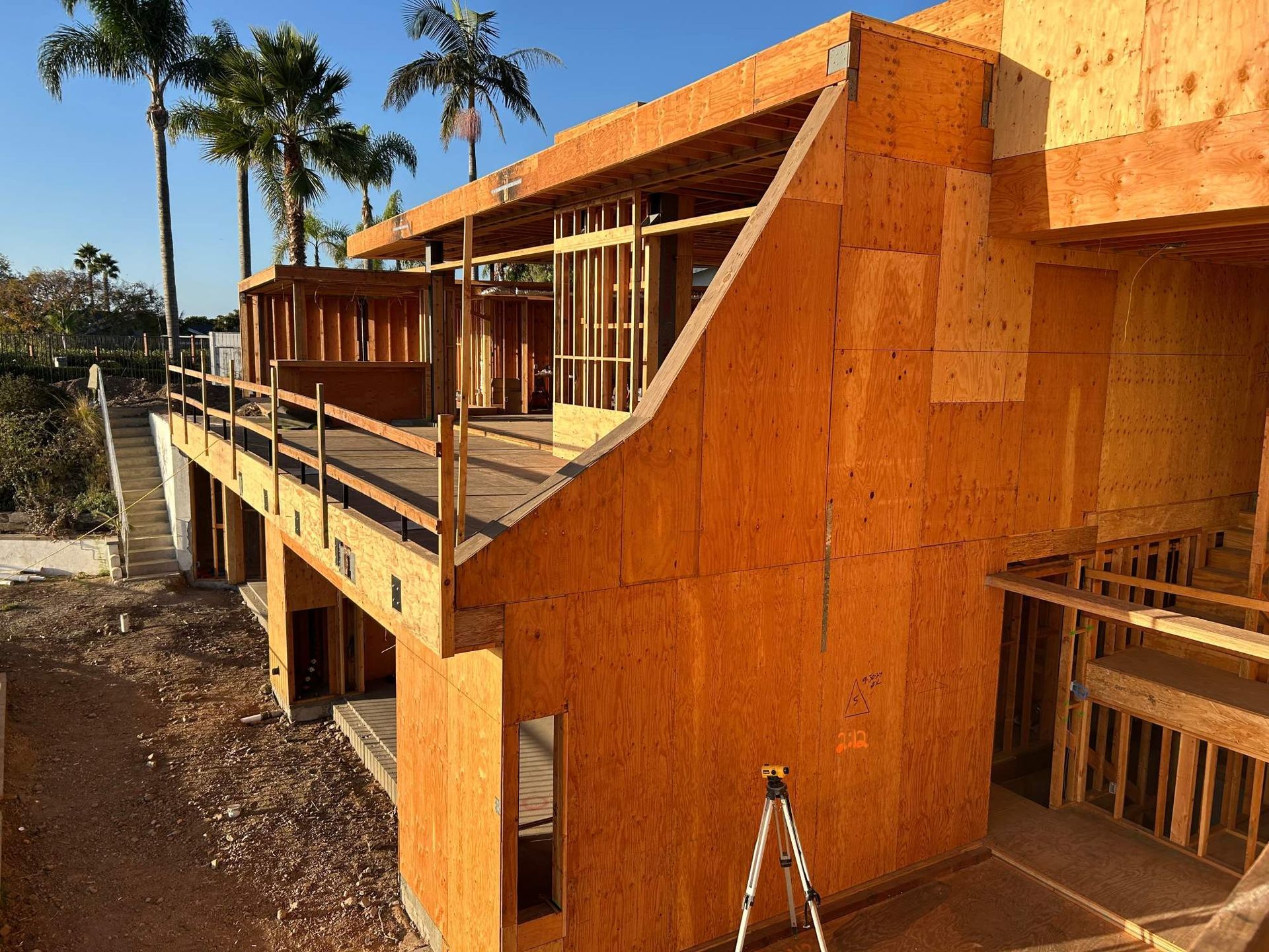 Orange wooden building under construction with a balcony and palm trees nearby