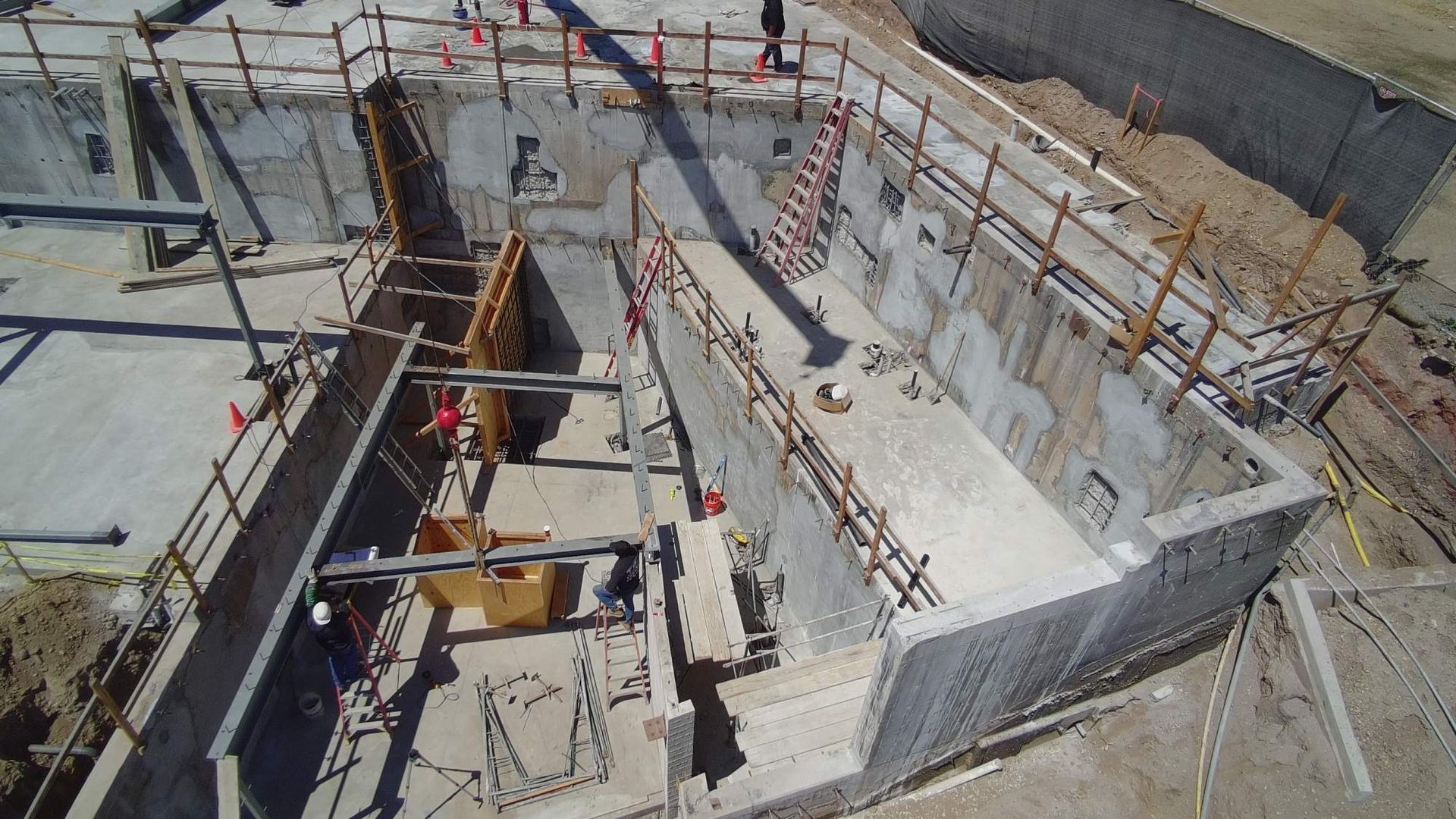 Construction site with workers in a concrete foundation trench and scaffolding around the perimeter