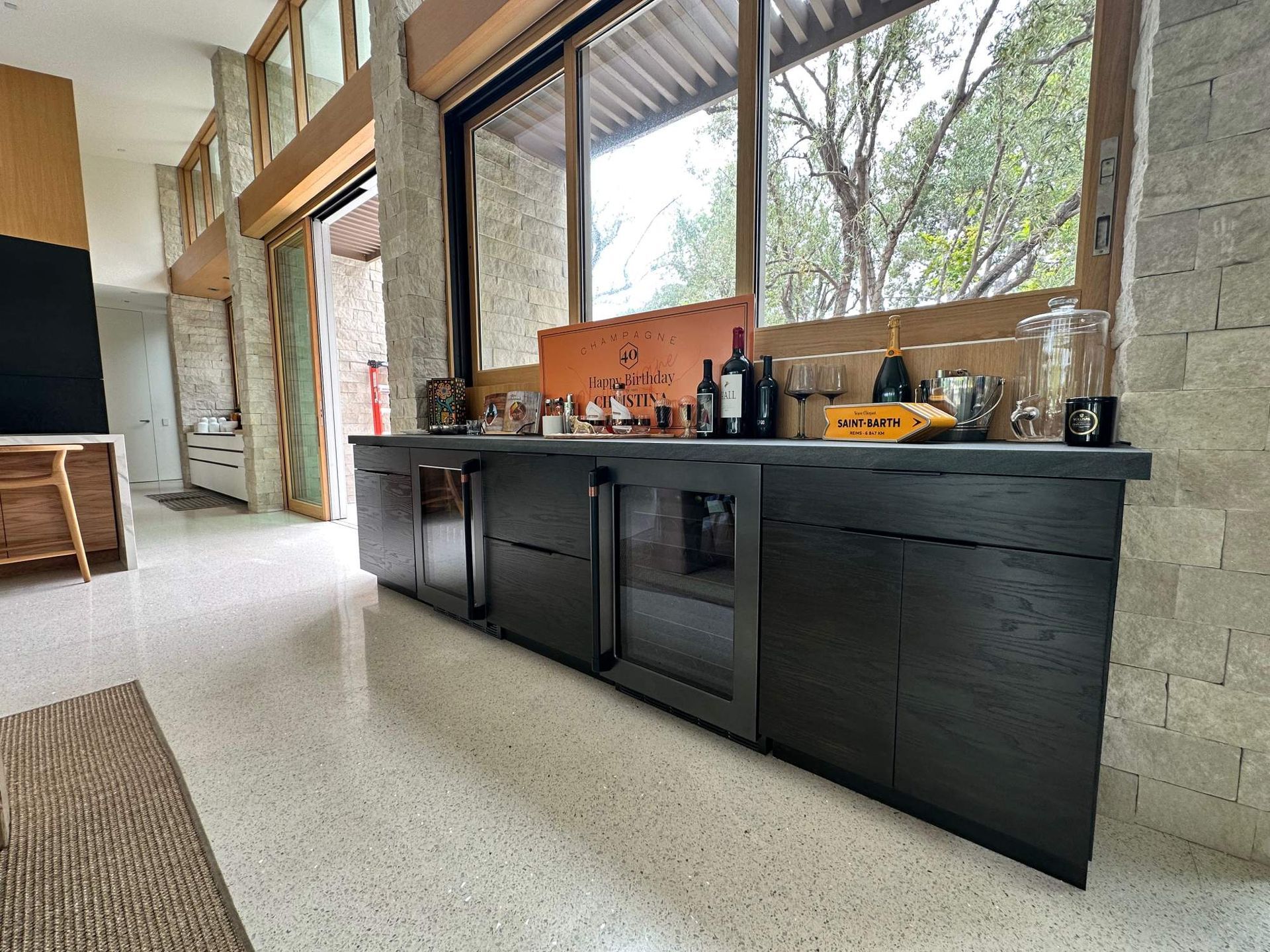 Modern kitchen with black cabinets, large windows, and a terrazzo floor in a bright open room