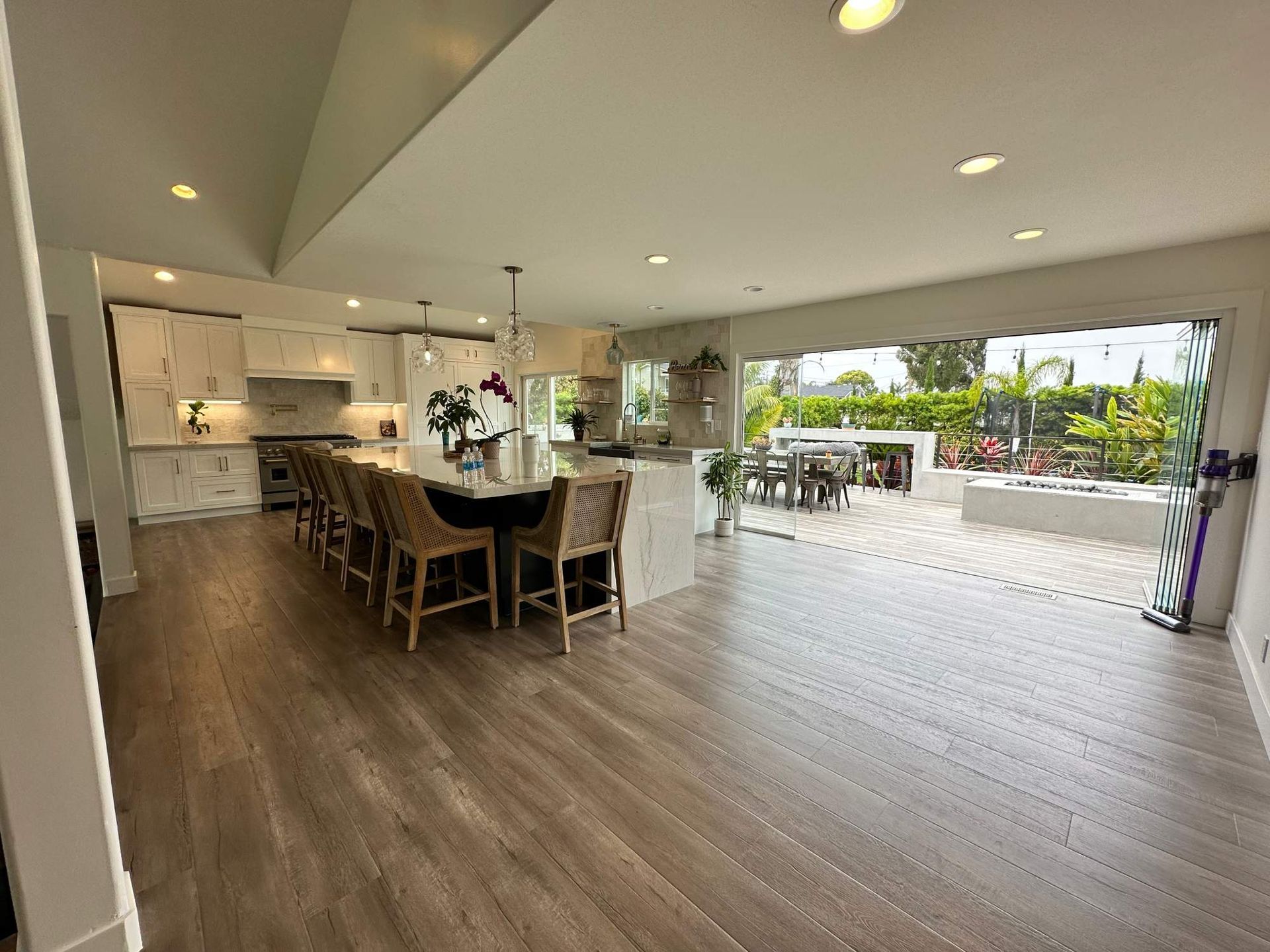 Open-concept kitchen and living area with large sliding doors opening to a sunny patio and outdoor seating