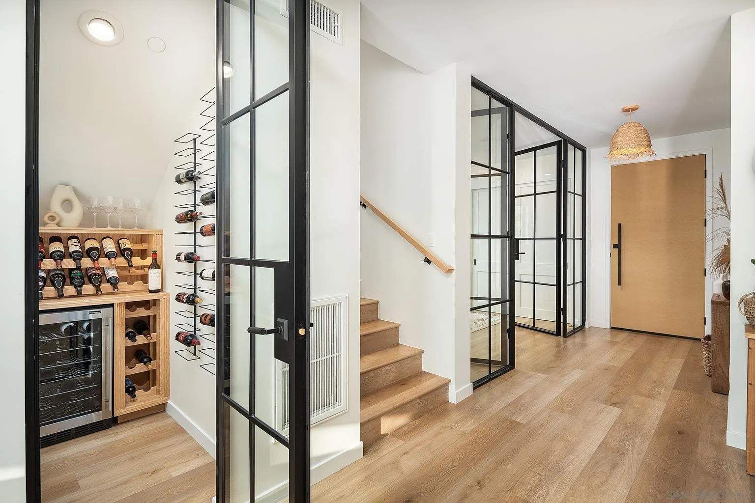 Bright modern hallway with wood floors, glass doors, staircase, and a wine rack on the left
