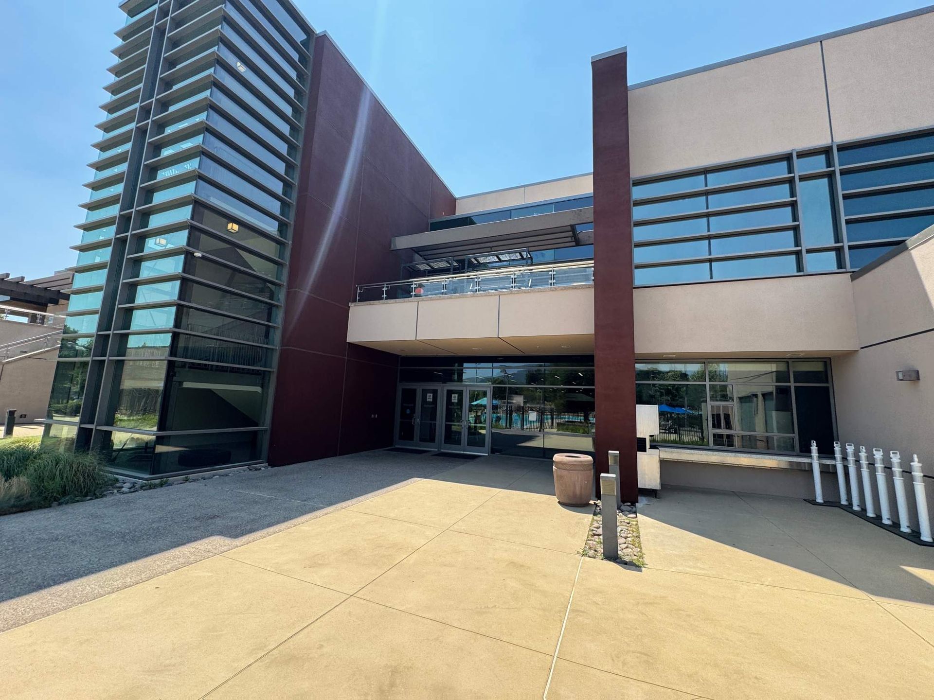 Modern building entrance with glass facade, beige walkway, and tall red-brown columns