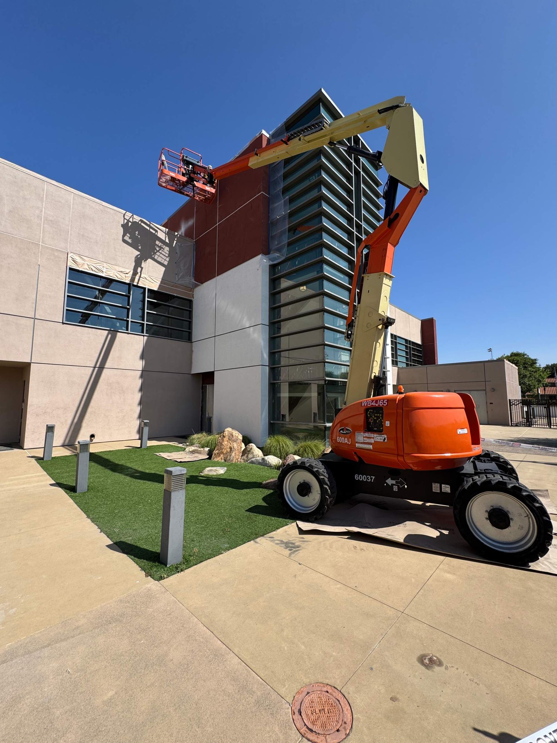 Orange boom lift beside a modern glass building under construction on a sunny day