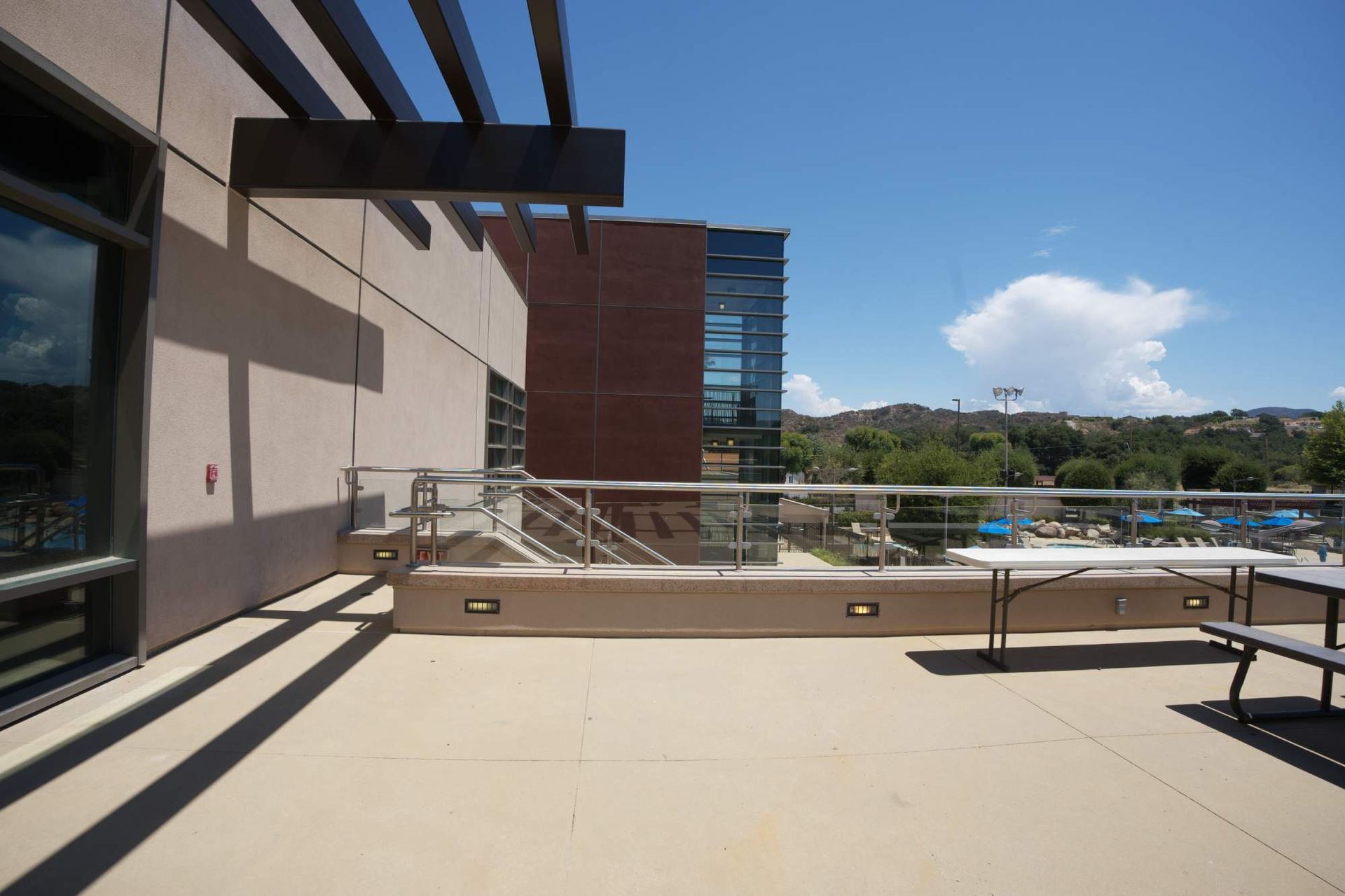 Sunny rooftop terrace with lounge chairs, railings, and a view of trees and mountains