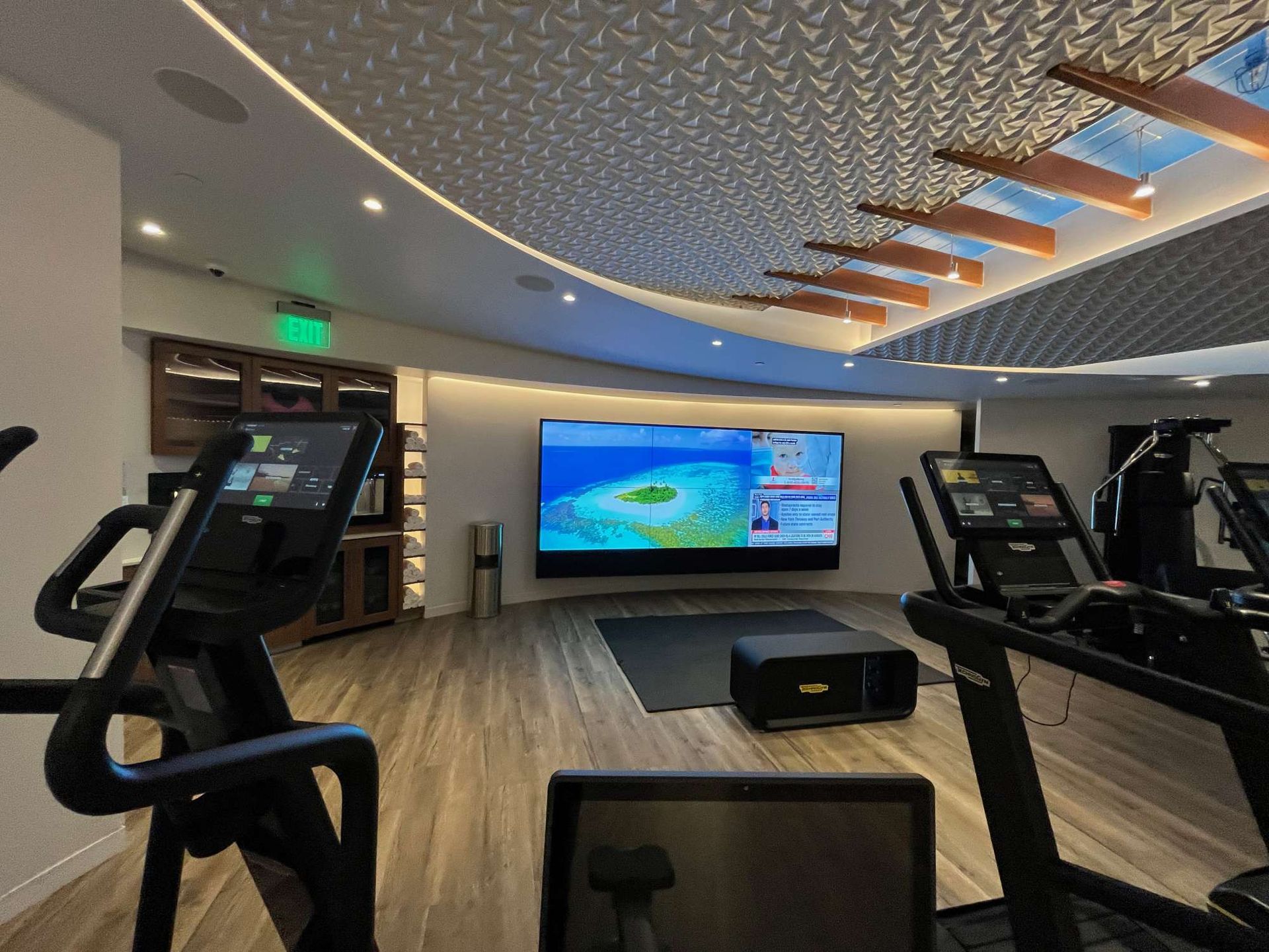 Modern gym with cardio machines, large wall screen, and curved LED ceiling lighting