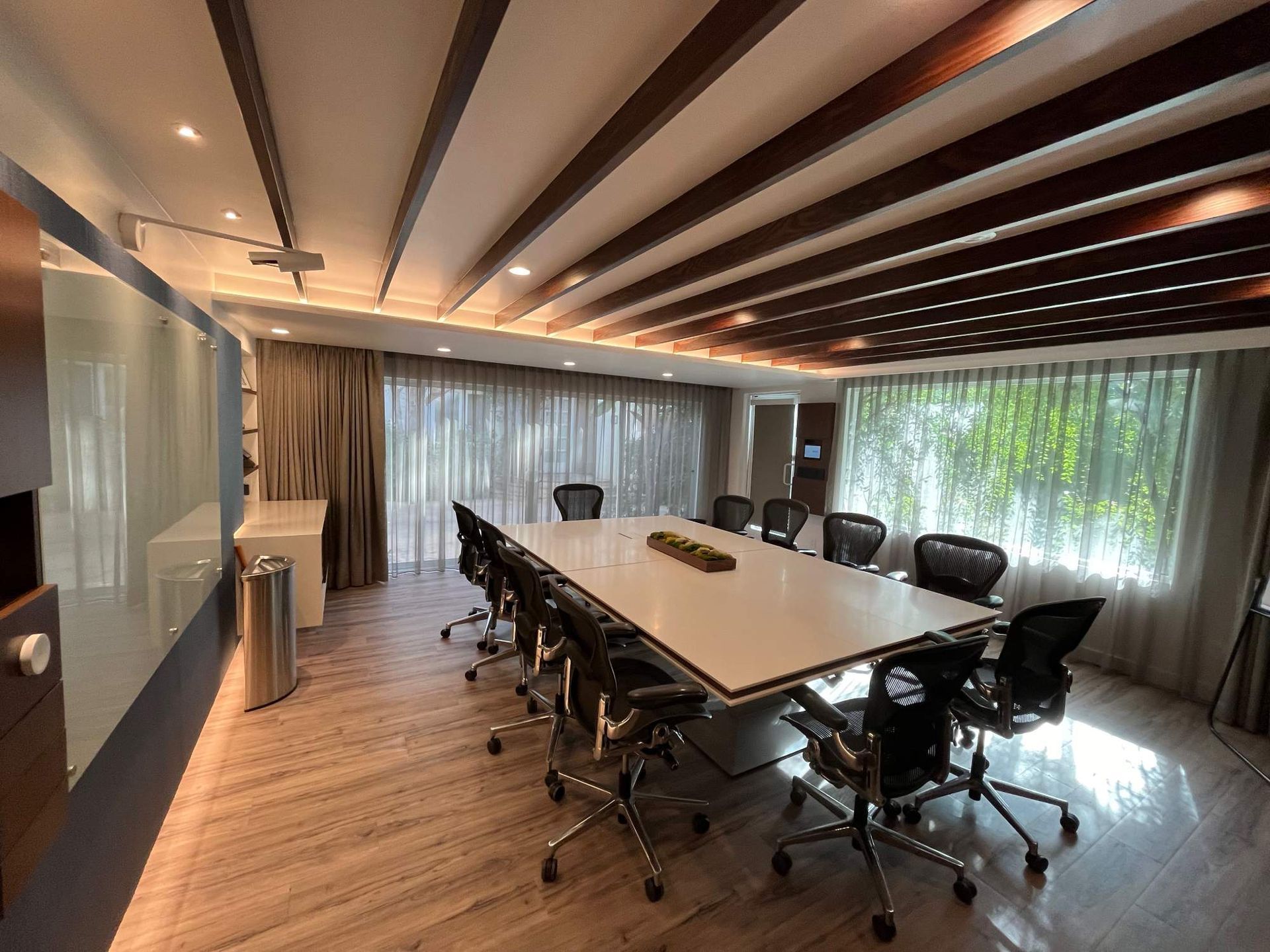 Modern conference room with long table, black chairs, wood floor, and floor-to-ceiling windows