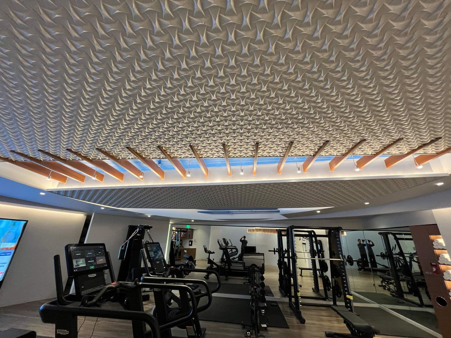 Modern gym interior with exercise machines, mirrors, and a textured ceiling with recessed lighting