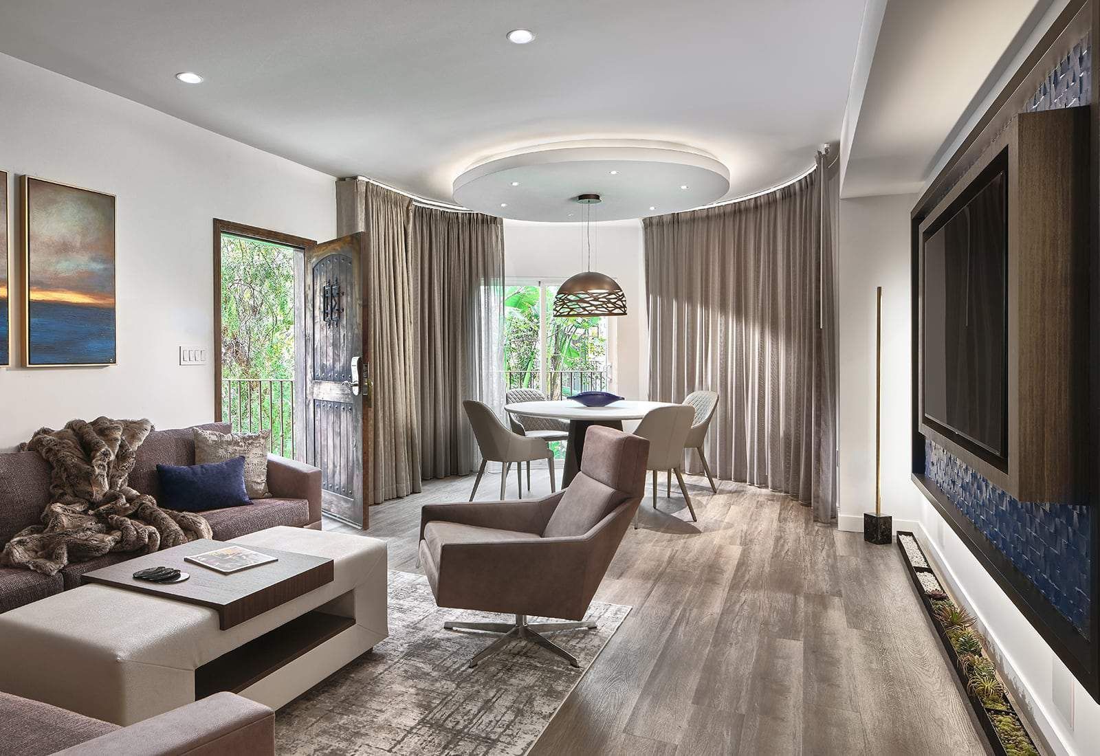 Modern living room with sectional sofa, lounge chair, round table, and large windowed curtains