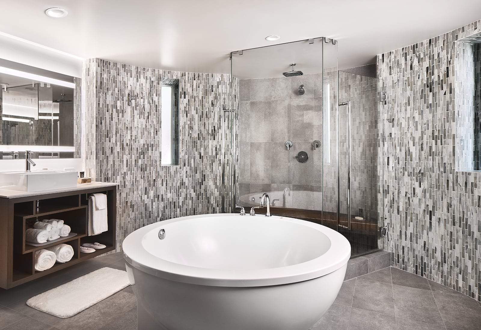 Modern bathroom with a freestanding tub, glass shower, vanity, and gray tile walls