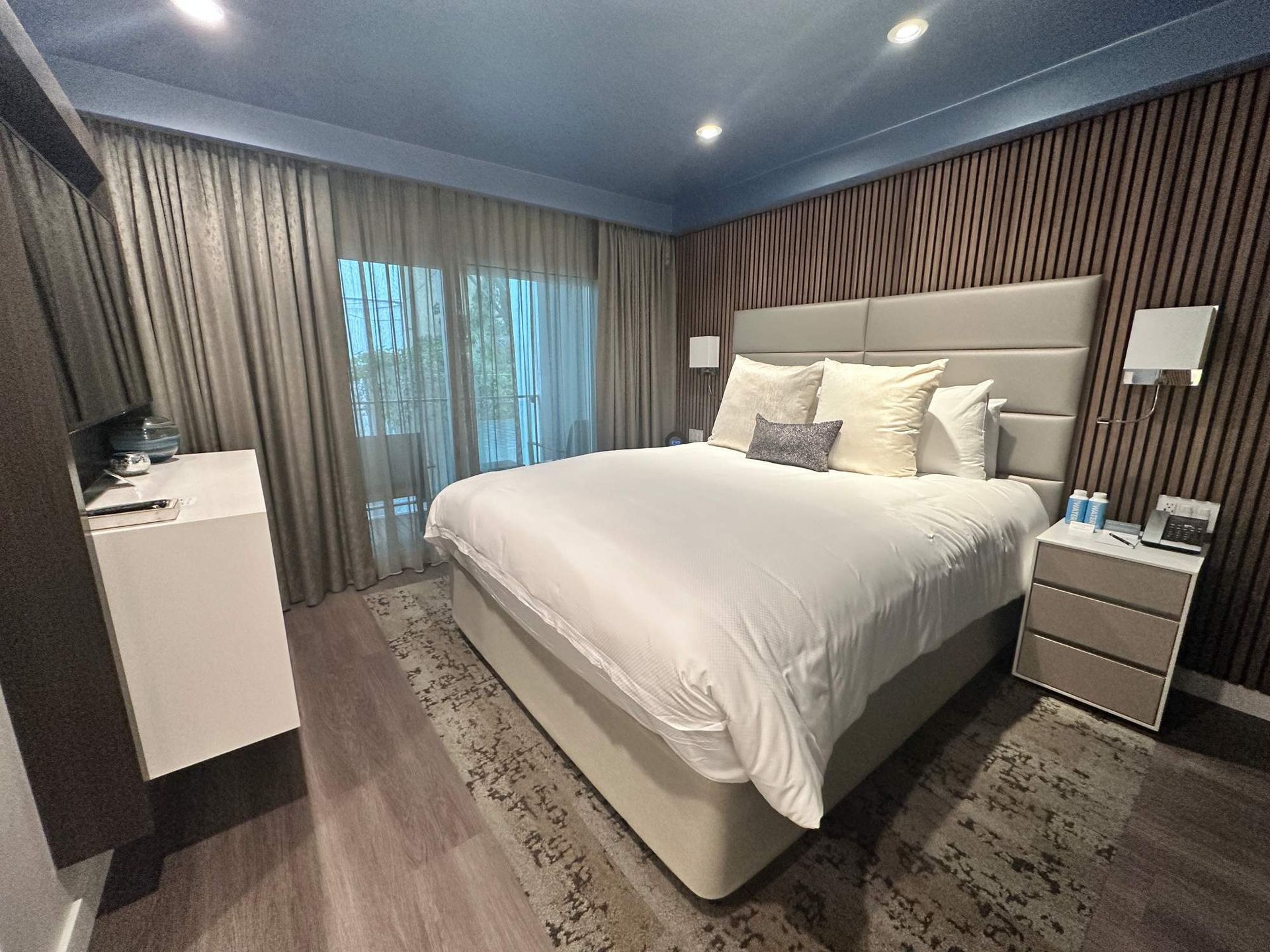 Modern bedroom with king bed, gray curtains, blue ceiling, and bedside tables