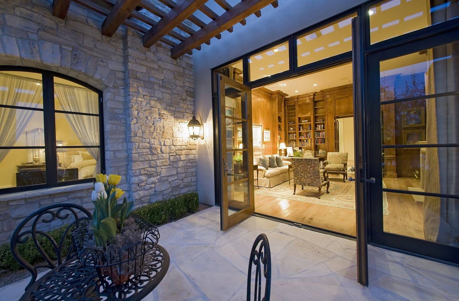 Stone patio with open French doors to a warmly lit living room at dusk