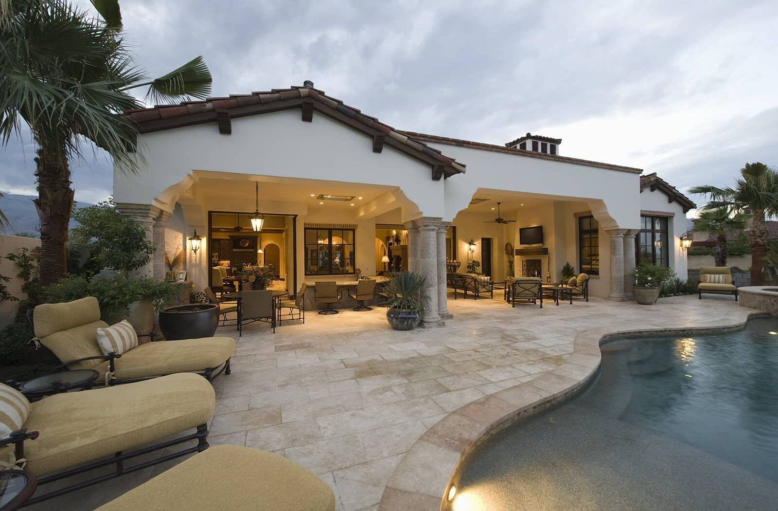 Luxury patio with lit seating area beside a swimming pool at dusk