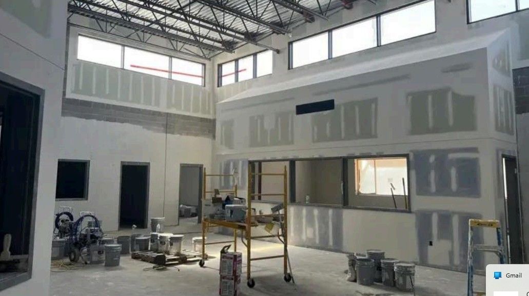 Interior of a large room under construction, with drywall, scaffolding, and tools scattered on the floor.