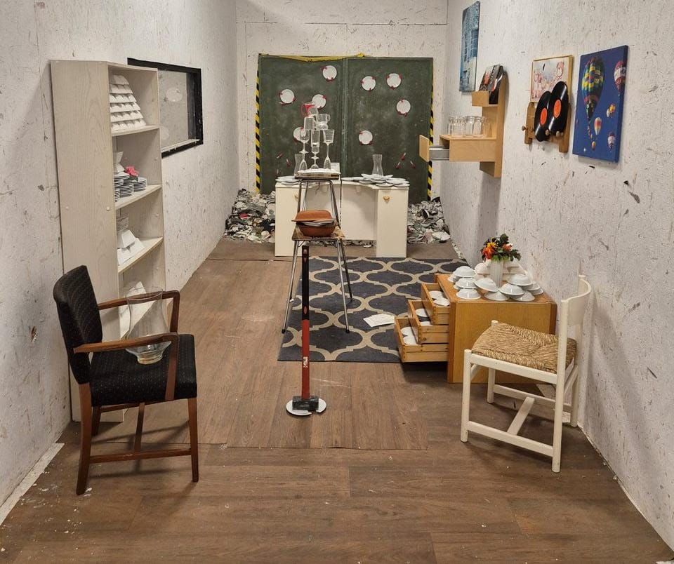 Kamer met oude meubels, versleten muren, een gedekte tafel en diverse decoratieve voorwerpen.