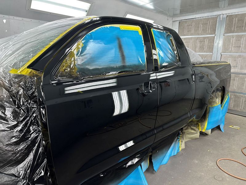 A black truck is being painted in a garage.